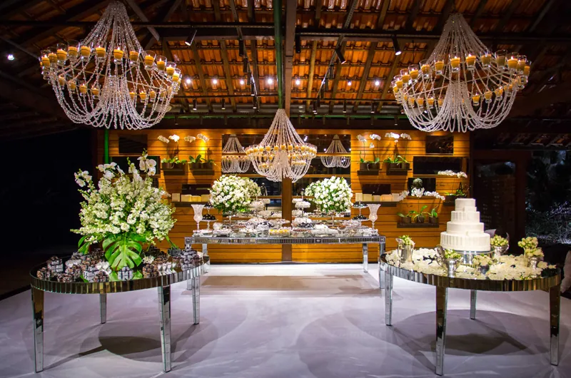 Salão do Lajedo com lustres, mesa de bolo e arranjos florais