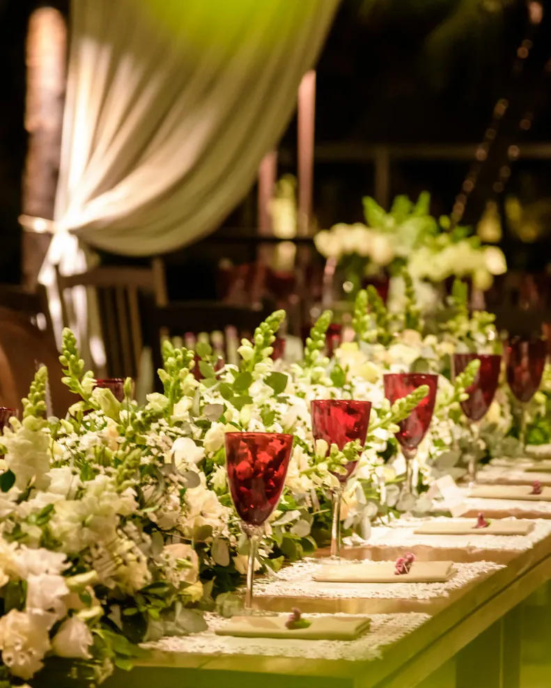 Mesa posta com flores brancas e taças em vermelho em um evento no Lajedo